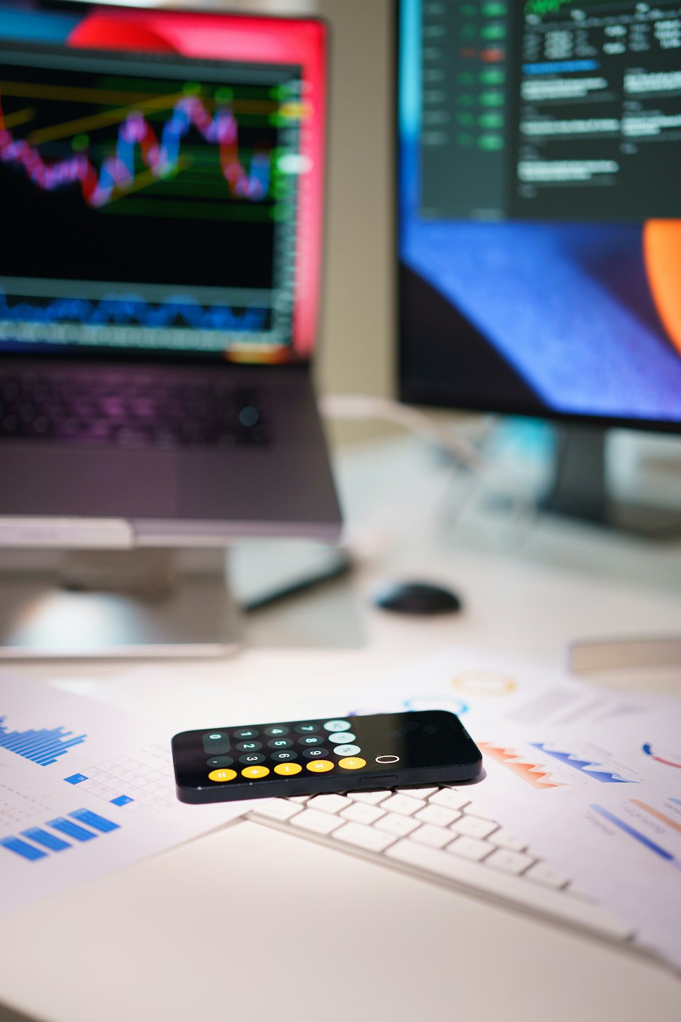 Servizi Smartphone su documenti finanziari vicino a un laptop con grafici azionari.