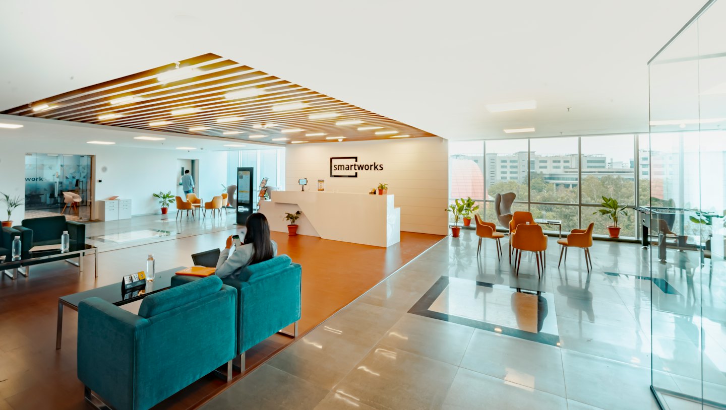 Contatti Donna su divano verde acqua usa il telefono in una reception moderna.