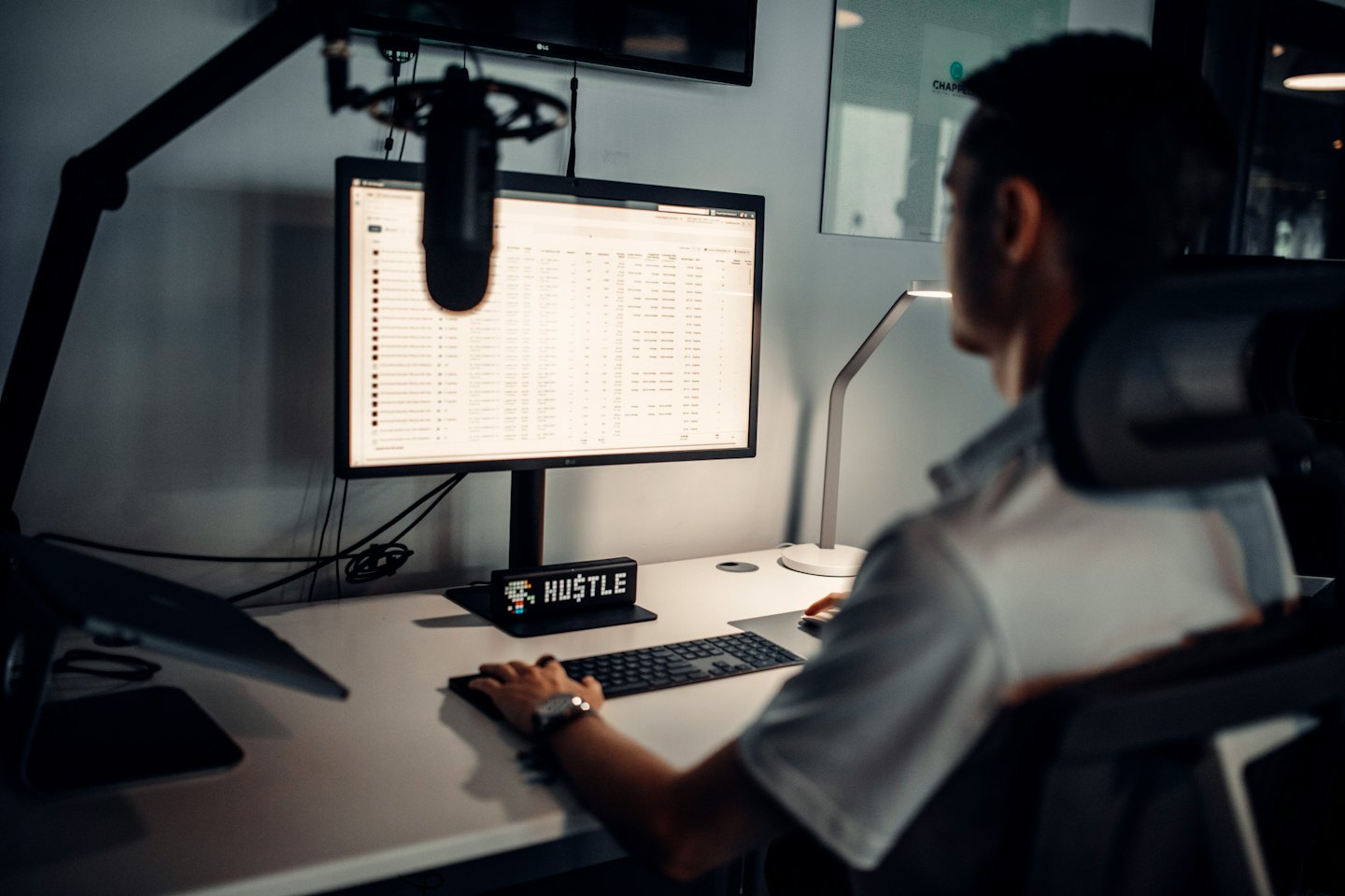 Home Persona che lavora al computer su una scrivania d'ufficio con un cartello 'HUSTLE'.